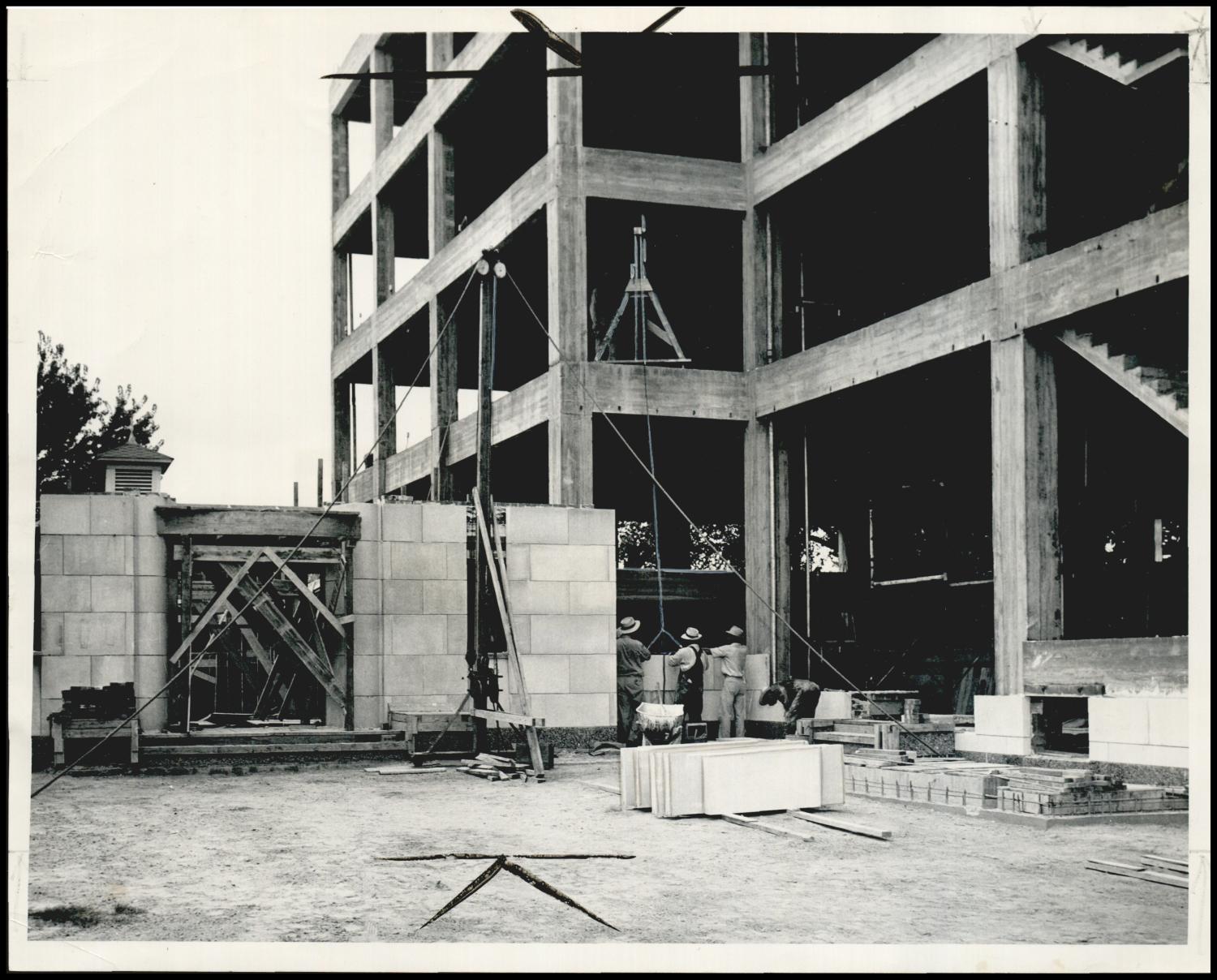July 1949: workers set limestone blocks for the auditorium wing while the concrete frame of the main building rises behind them