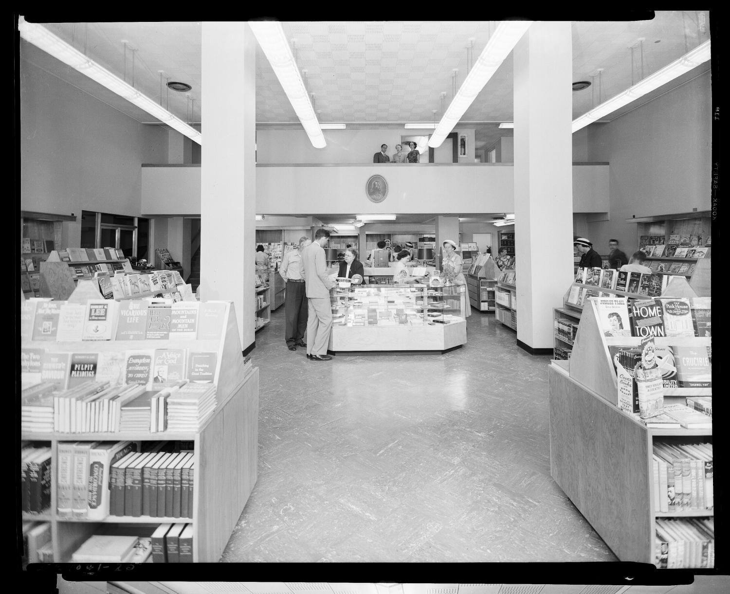 May 1950: the first-floor bookstore, with book displays, a glass counter, customers browsing, and a mezzanine above