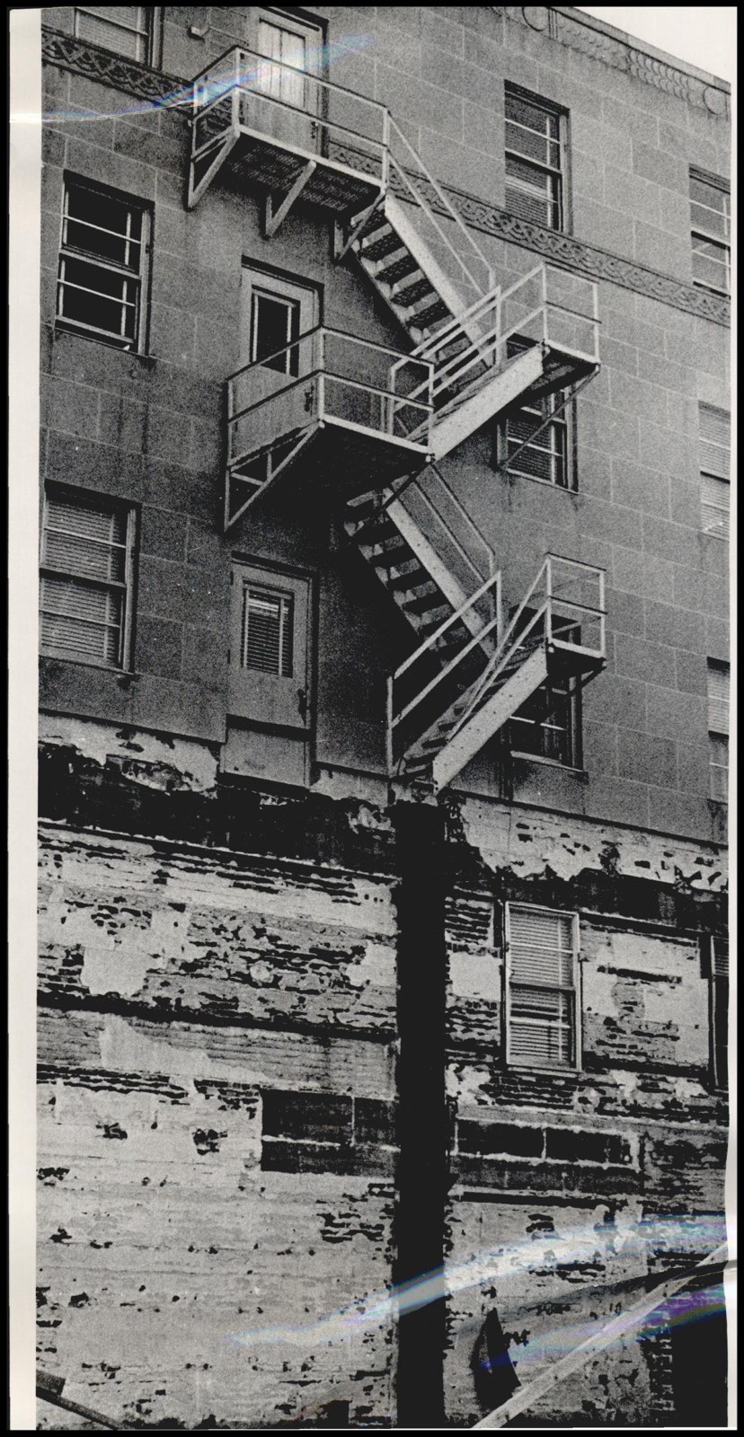 November 1964: a zigzag steel fire escape on the limestone rear wall, with the lower courses of stone stripped and deteriorating